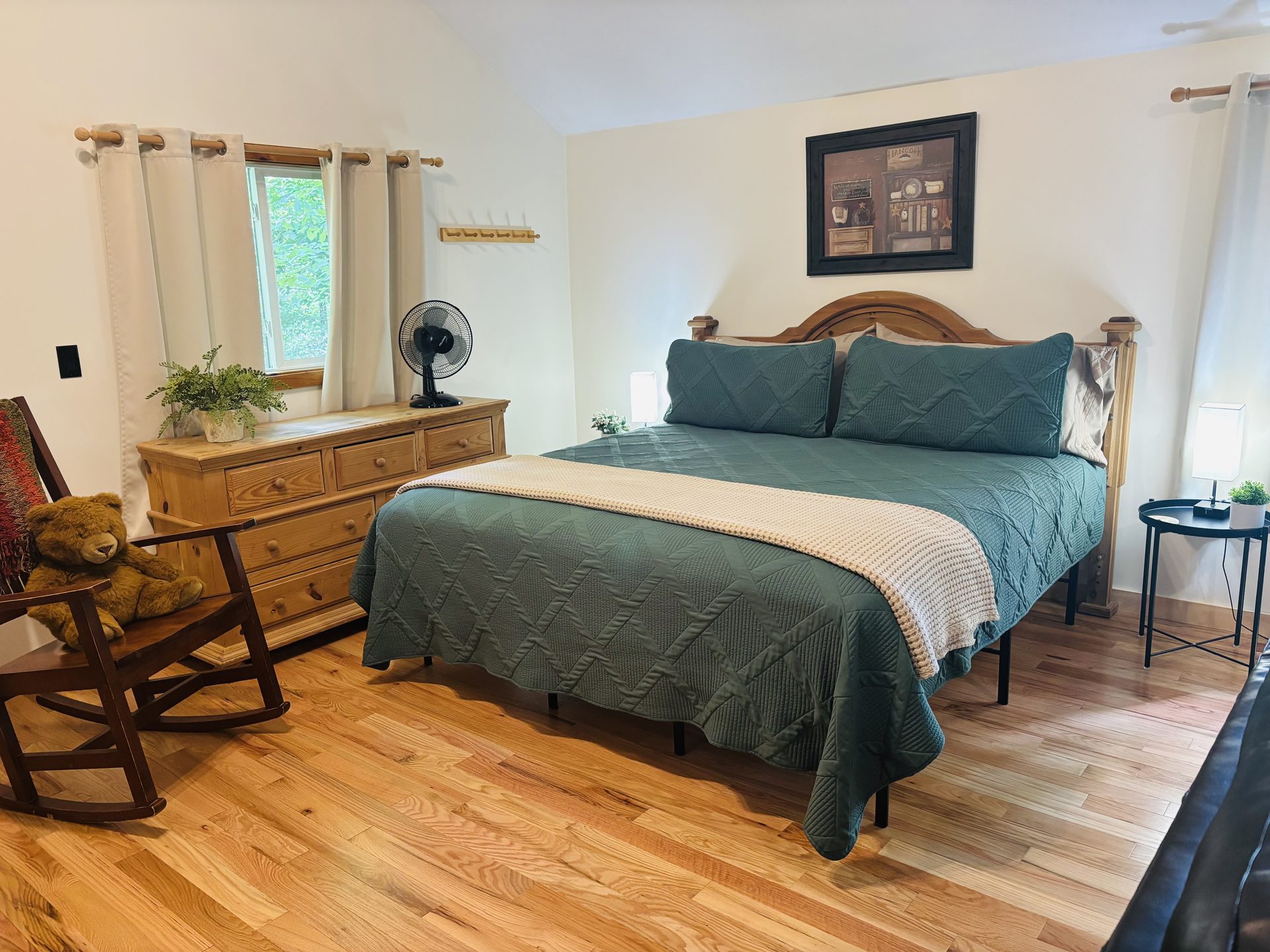 King bed with a green quilt beside a pine dresser at Sugar Maple Cabin