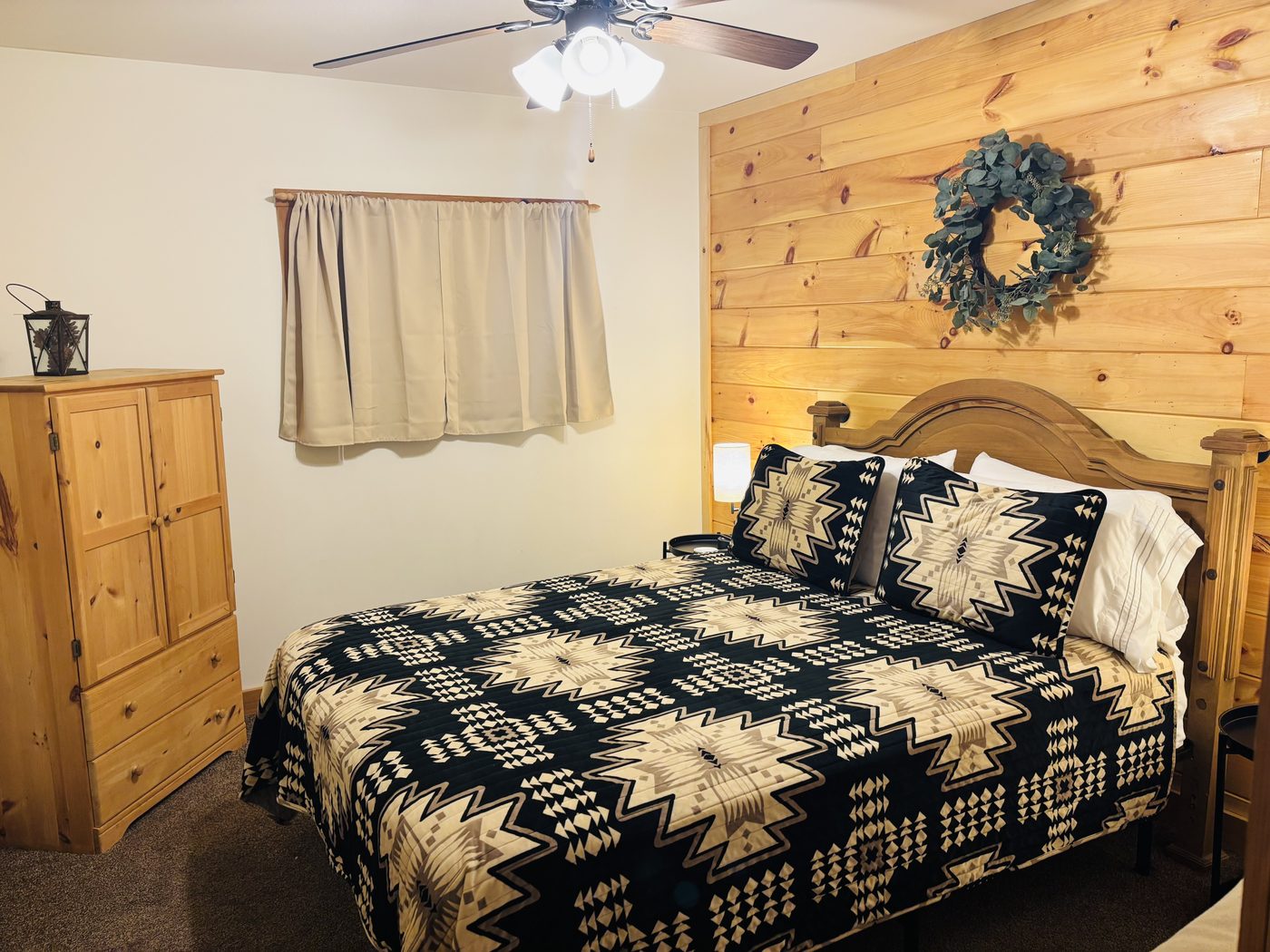 A bedroom at Red Oak Cabin with a pine accent wall, patterned quilt and pine armoire