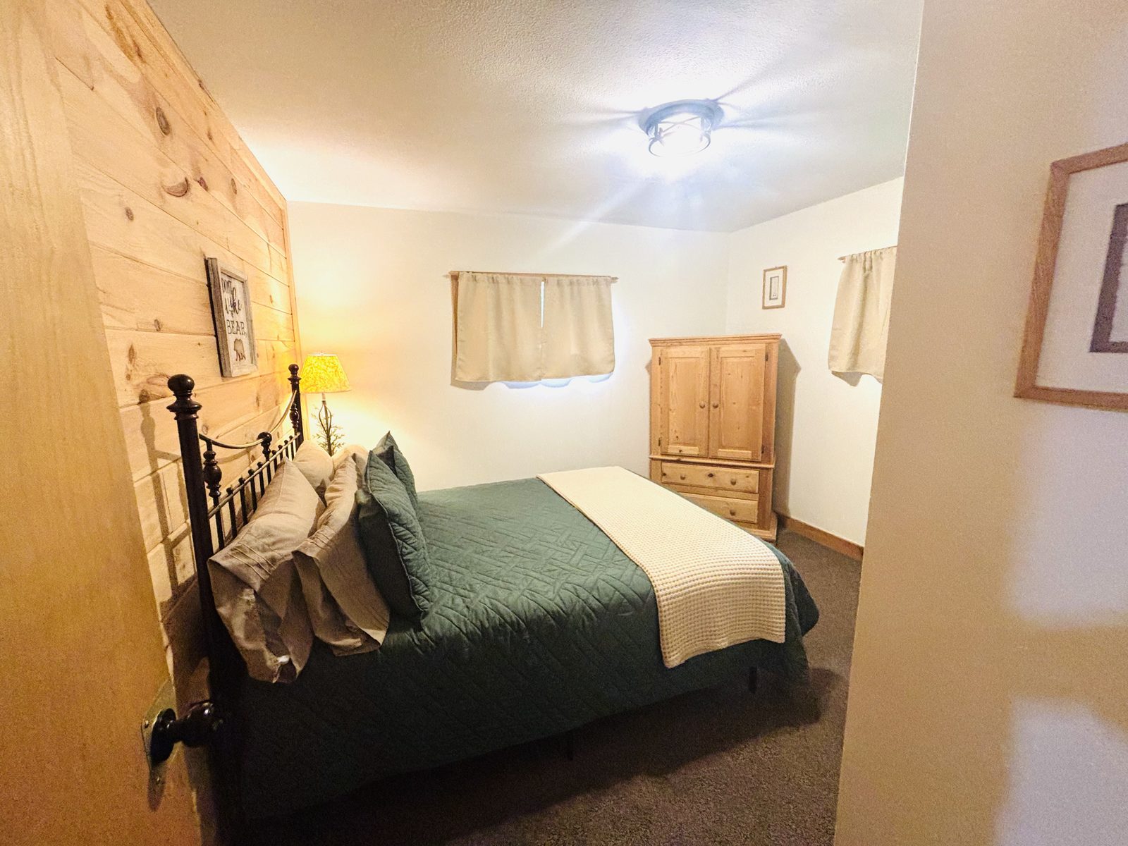 A bedroom at Red Oak Cabin with a black iron bed, green quilt and bedside lamp