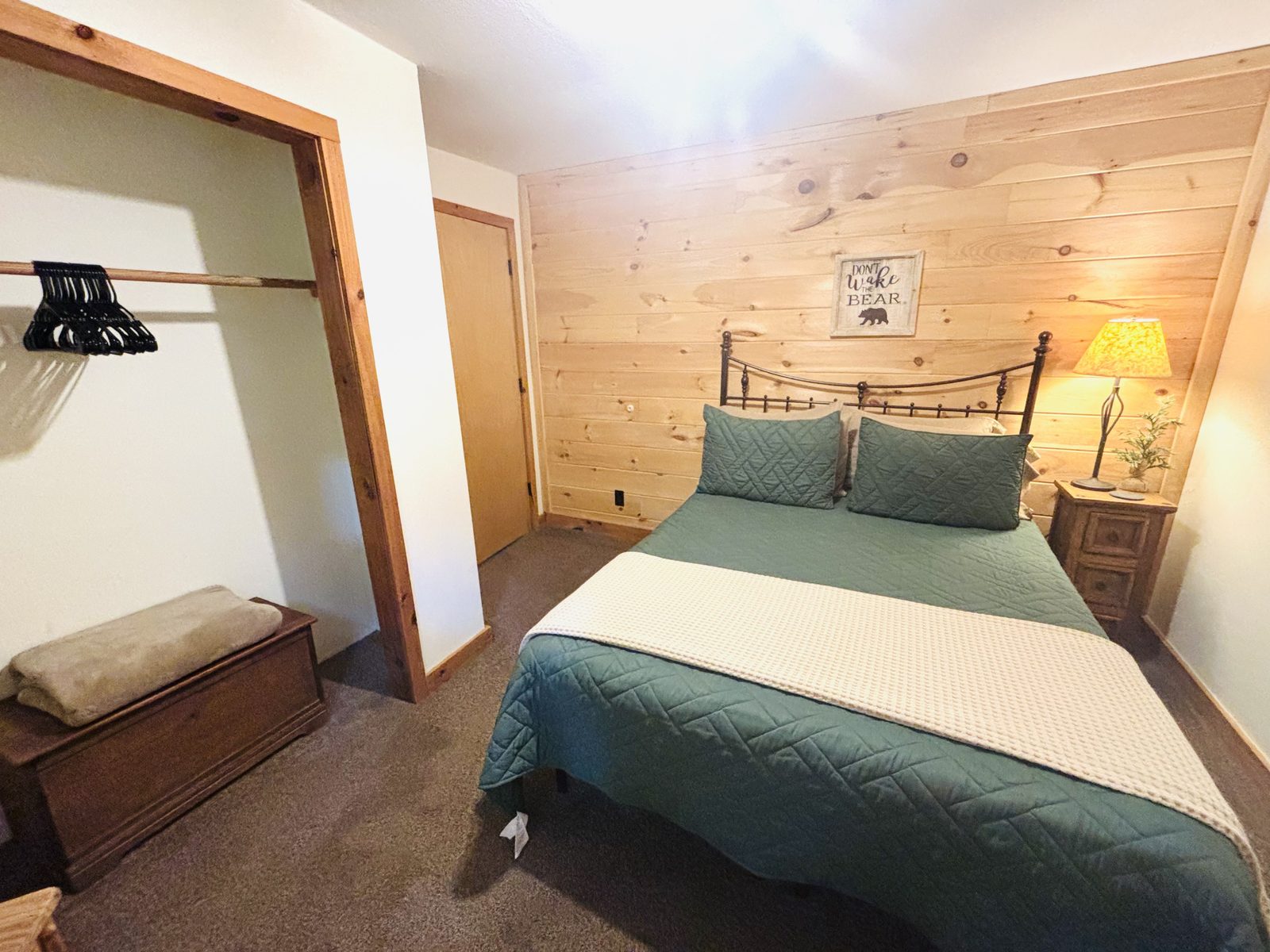A bedroom at Red Oak Cabin with a teal quilt, iron bed and open hanging space