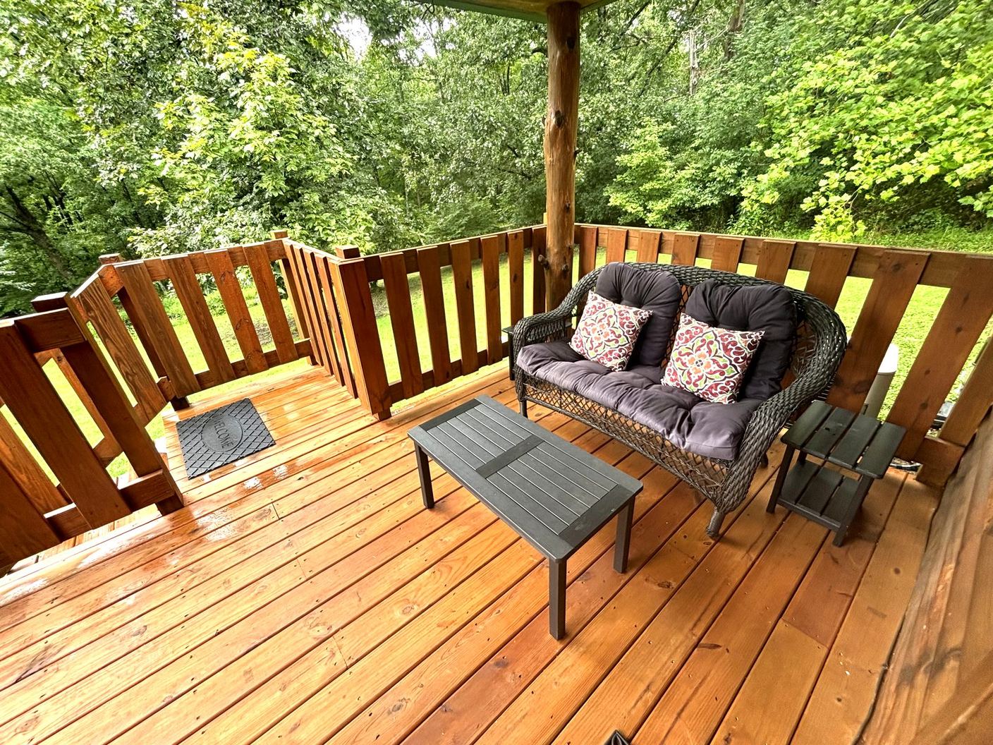 A cushioned wicker loveseat on the covered deck at Red Oak Cabin, looking into the trees