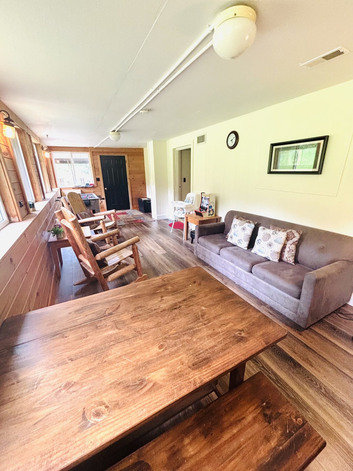 Sofa and long wooden table in the sun room at Red Oak Cabin, windows on three sides