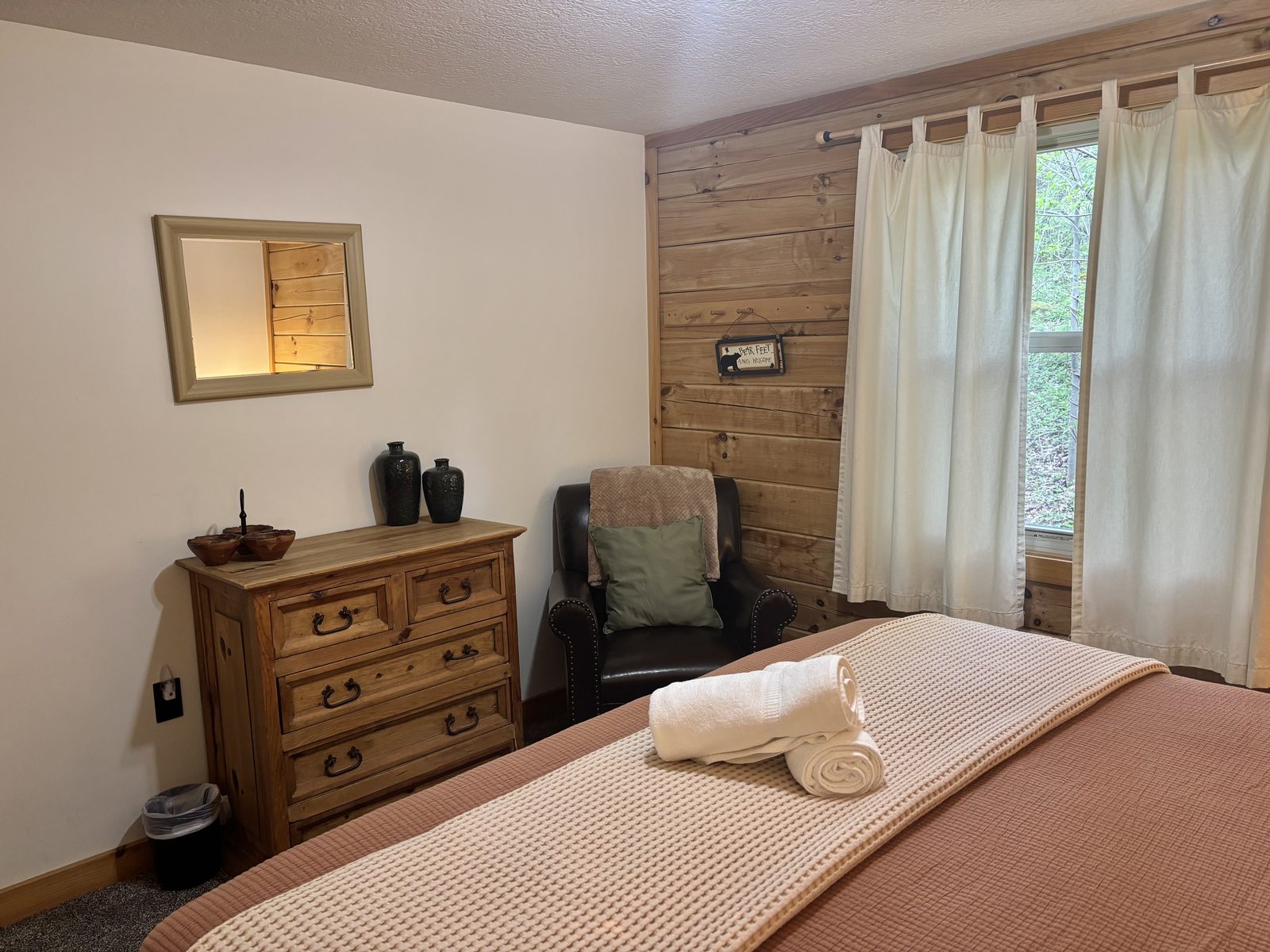 A downstairs bedroom at Redbud Cabin, rust bedding and a pine dresser with a leather armchair by the window