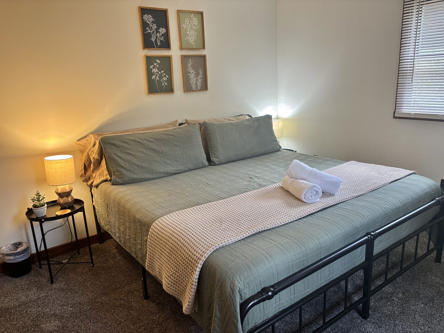 A downstairs bedroom at Redbud Cabin, sage bedding and botanical prints with a reading lamp