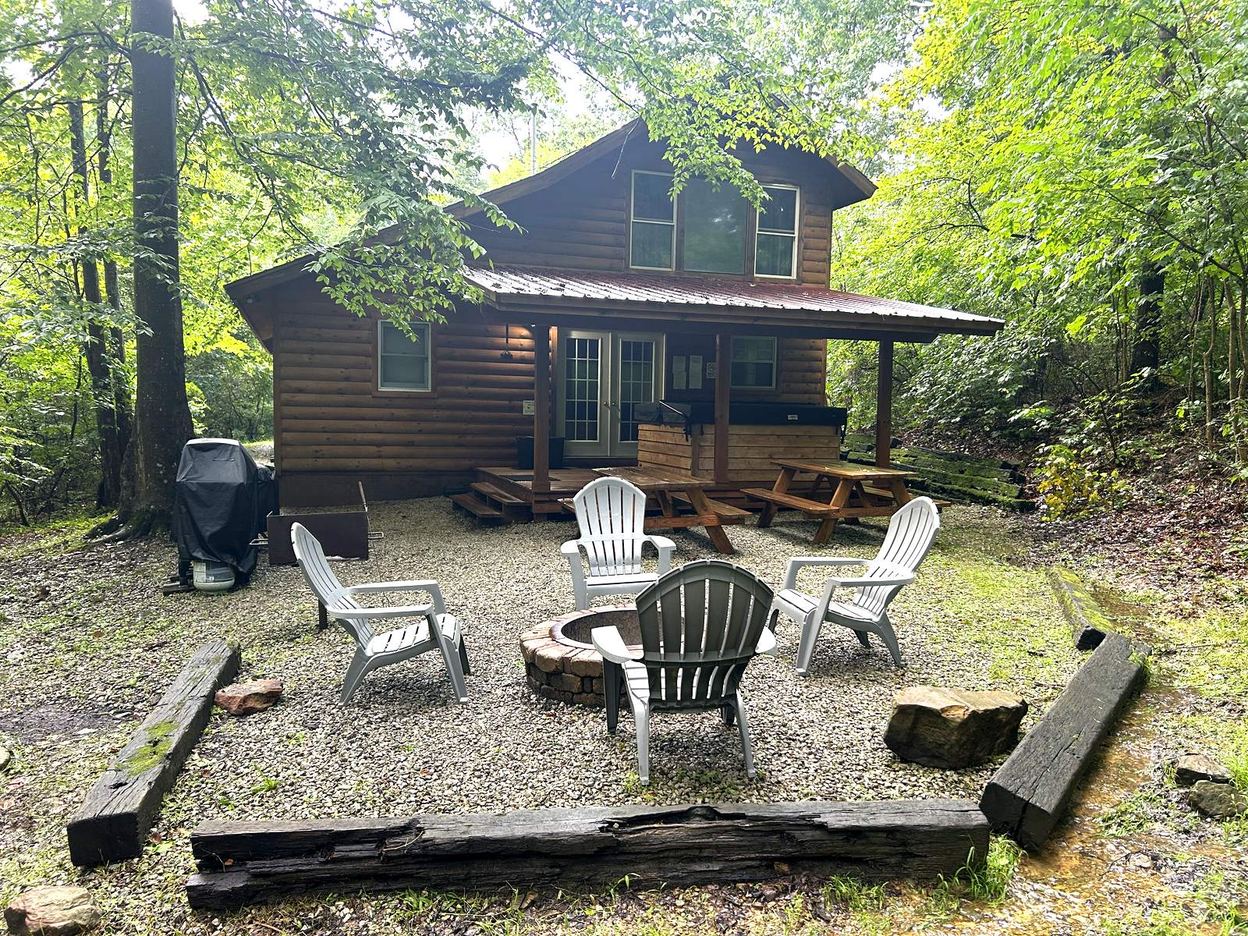 Stone fire ring and Adirondack chairs in the woods behind Redbud Cabin