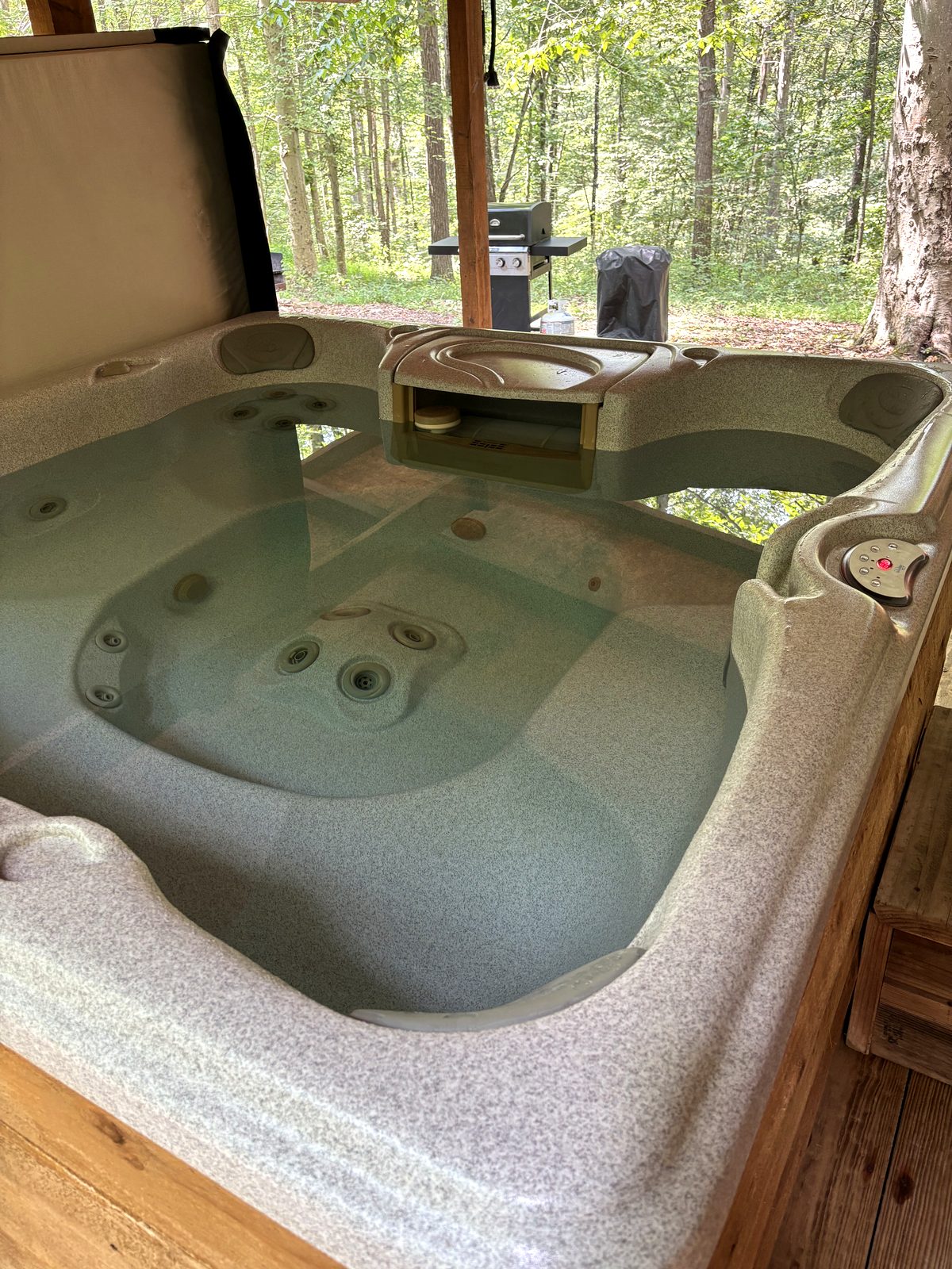 The hot tub on the covered deck at Redbud Cabin, open and looking into the woods