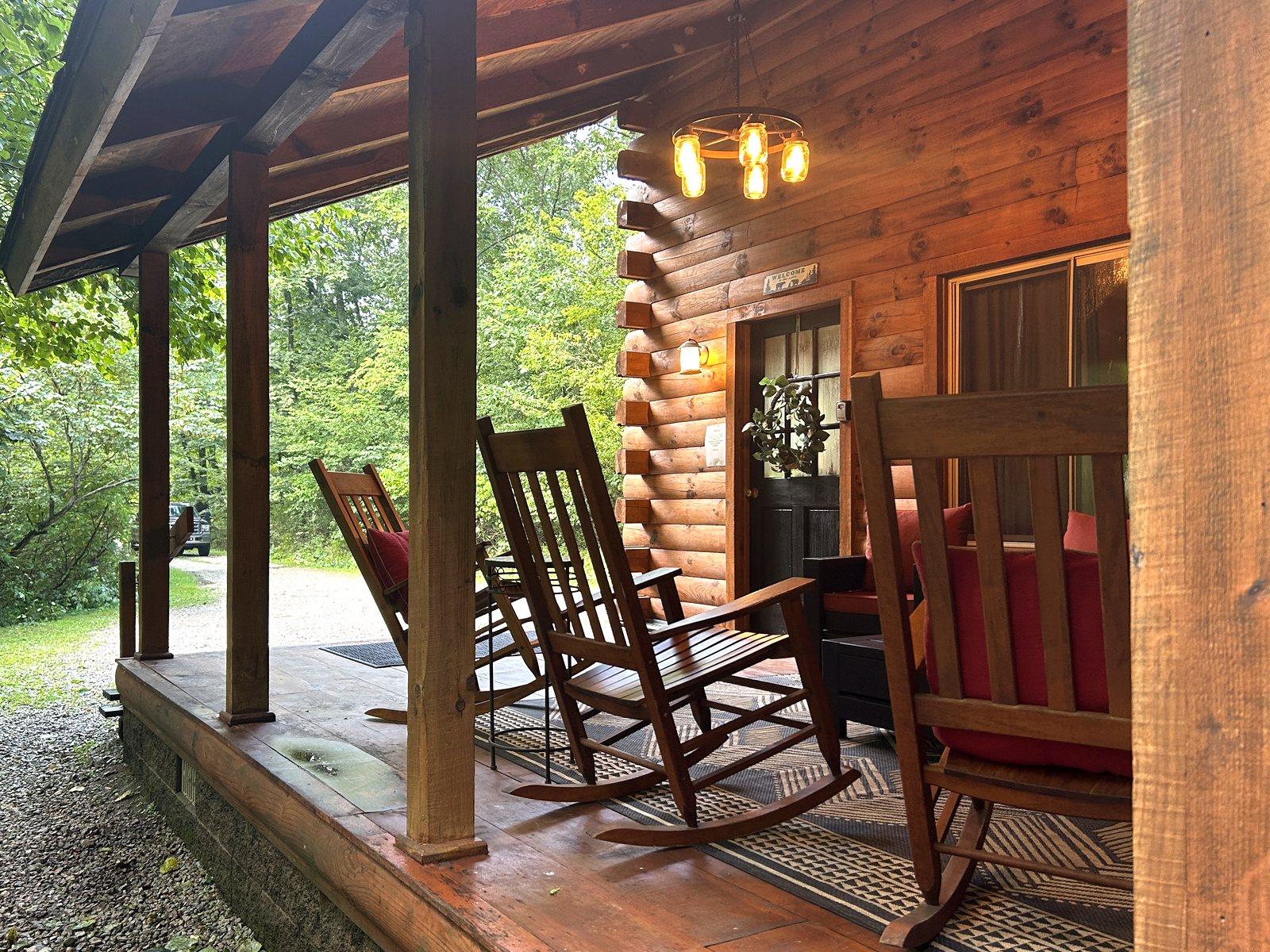 Rocking chairs and cushioned seating on the covered front porch at Redbud Cabin, lanterns lit