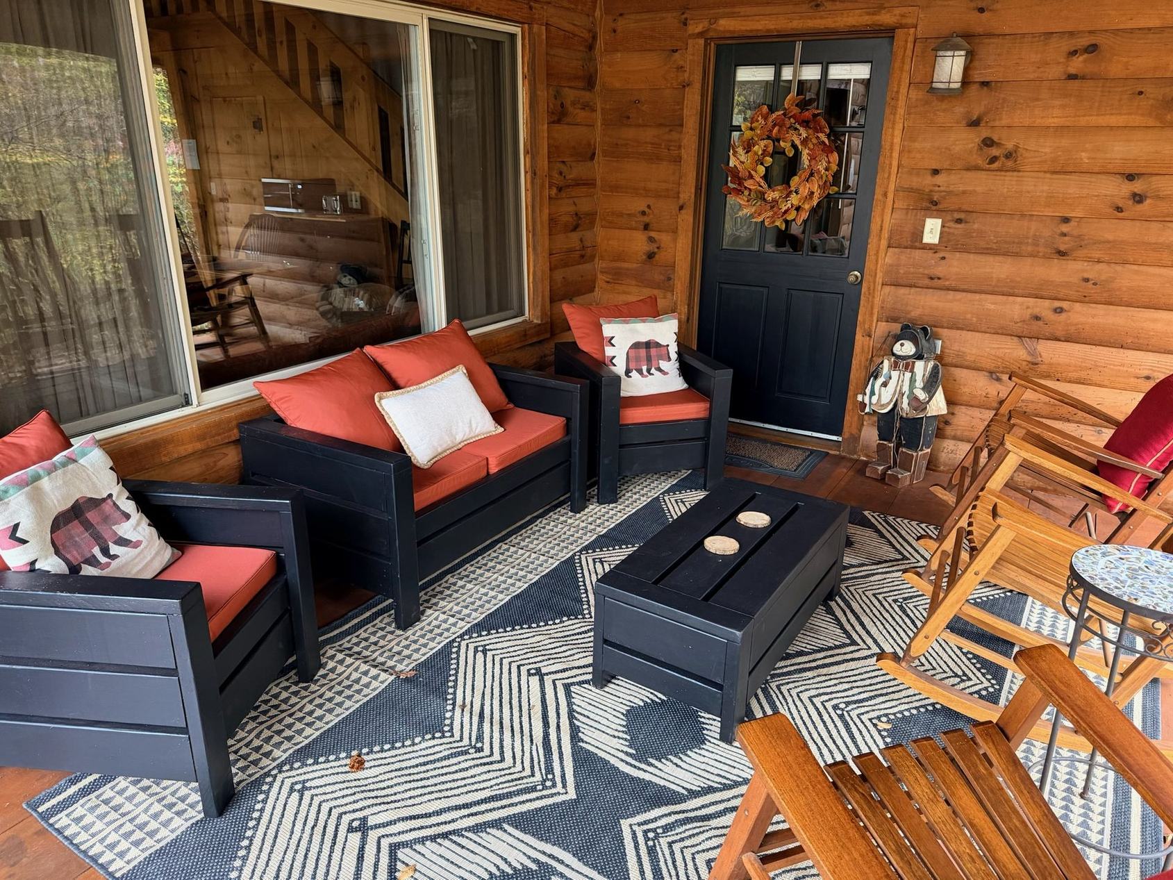 A covered cabin porch at Bear Run with rocking chairs, cushioned seating and the woods beyond