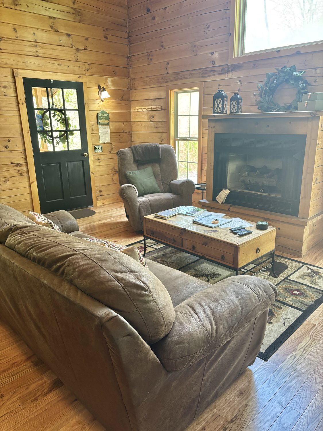 The living room at Redbud Cabin looking toward the stone-hearth gas fireplace and the front door, tall pine walls above