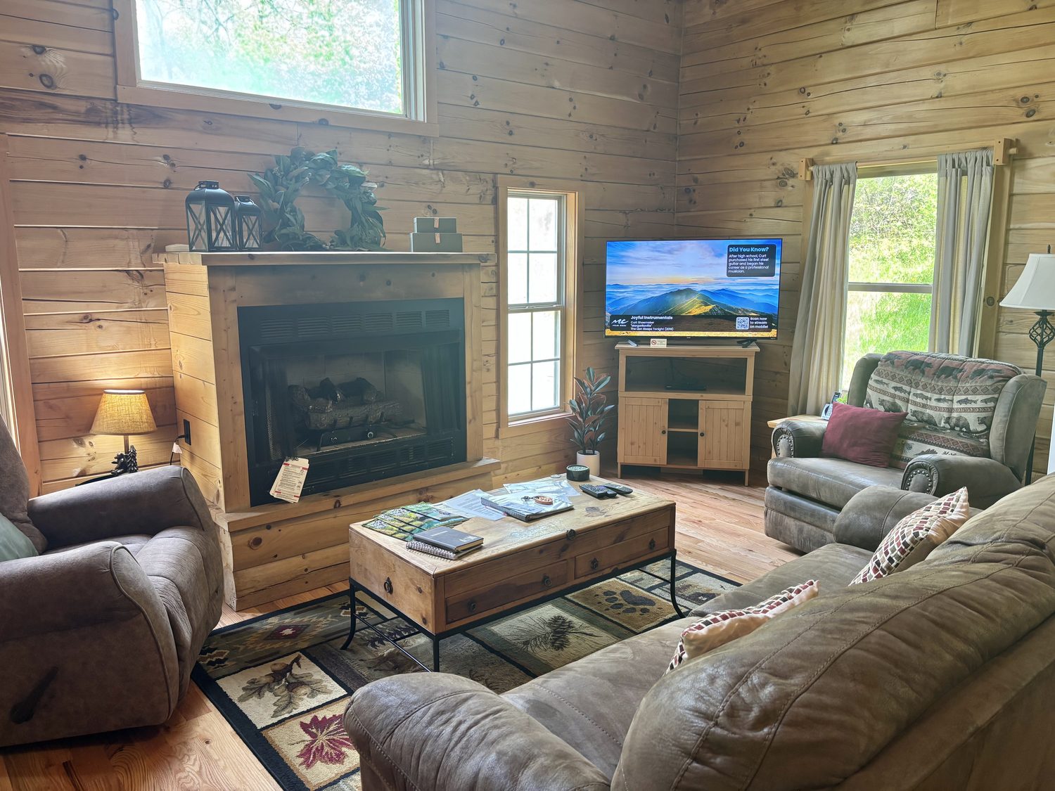 The living room at Redbud Cabin &mdash; gas fireplace, television, a leather sofa and two recliners under pine walls