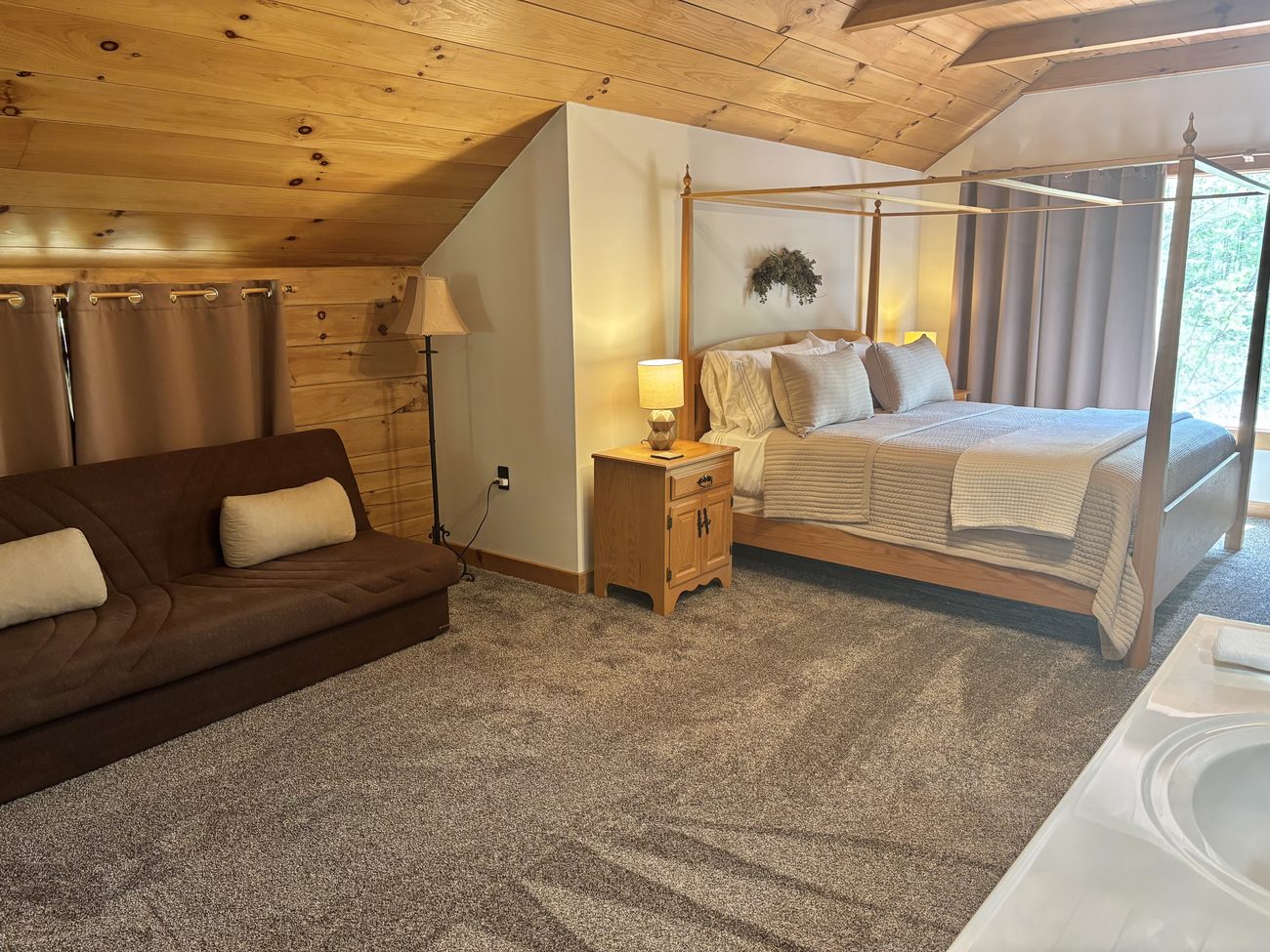 The upstairs master suite at Redbud Cabin under its pine ceiling &mdash; king four-poster bed, a full-size futon and the corner jacuzzi