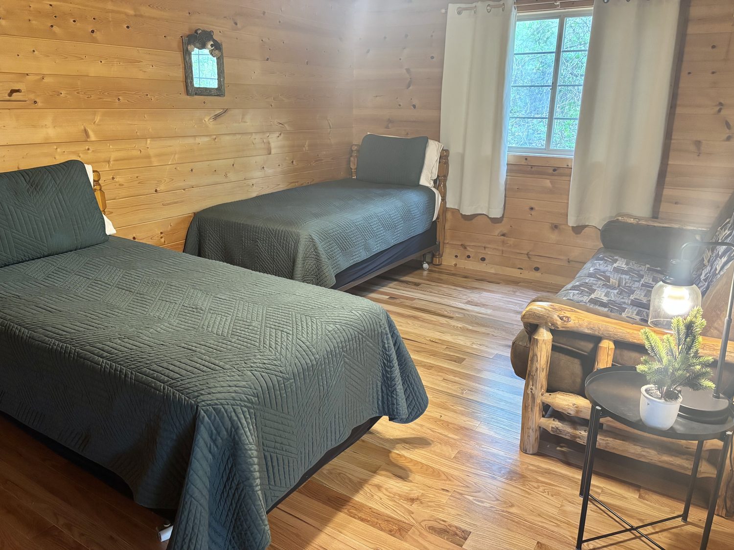 The twin-bedded room at Redbud Cabin &mdash; two twin beds in green quilts against pine panelling, with a log-frame queen sleeper sofa by the window