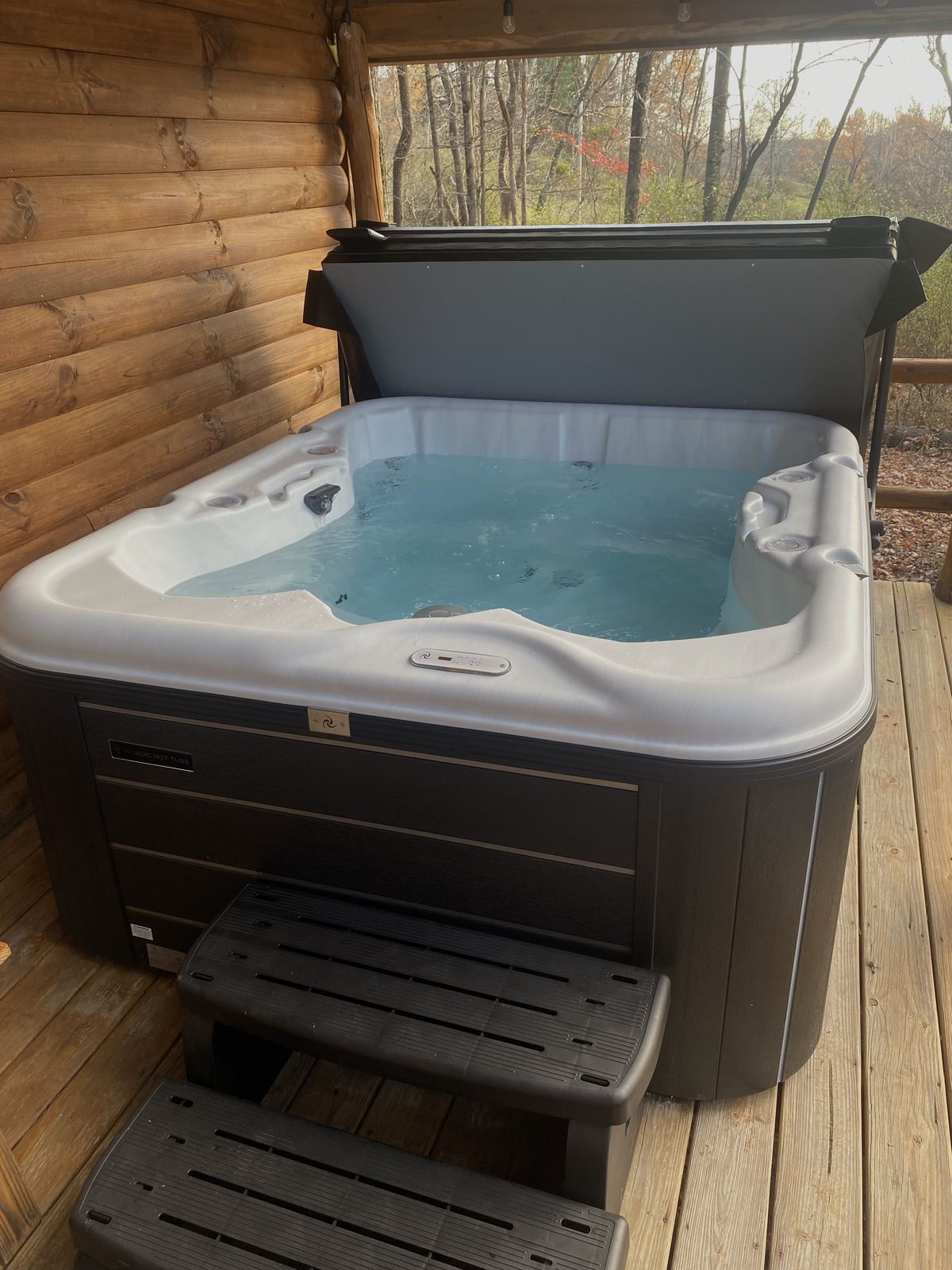 The private outdoor hot tub on the covered deck at Sugar Maple Cabin, clear water with autumn woods beyond